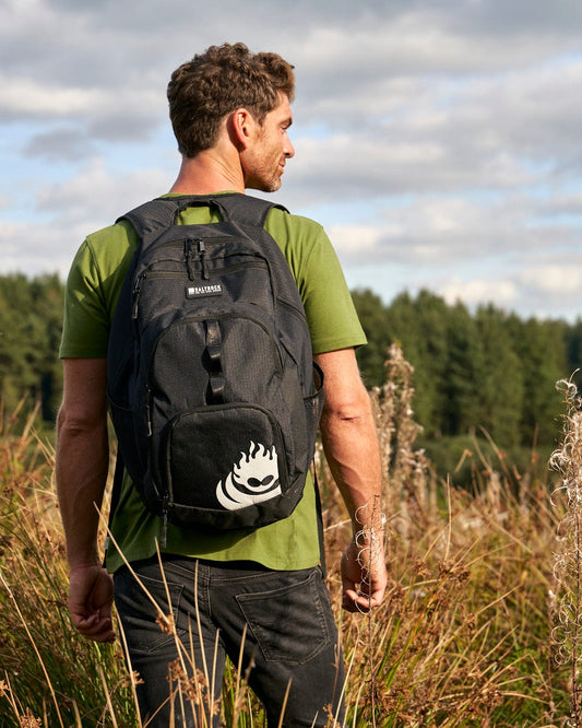 A man standing in a field with a Saltrock Boardwalk - Black Backpack.
