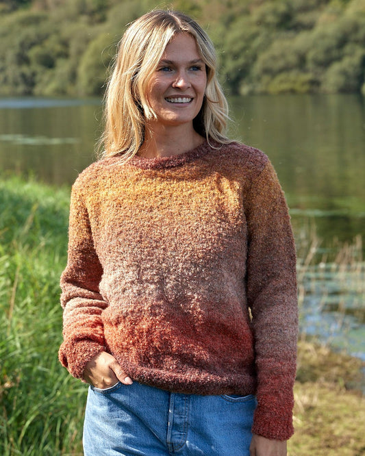 A woman wearing a Saltrock Bowden - Boucle Crew Jumper - Orange and jeans standing by a lake.