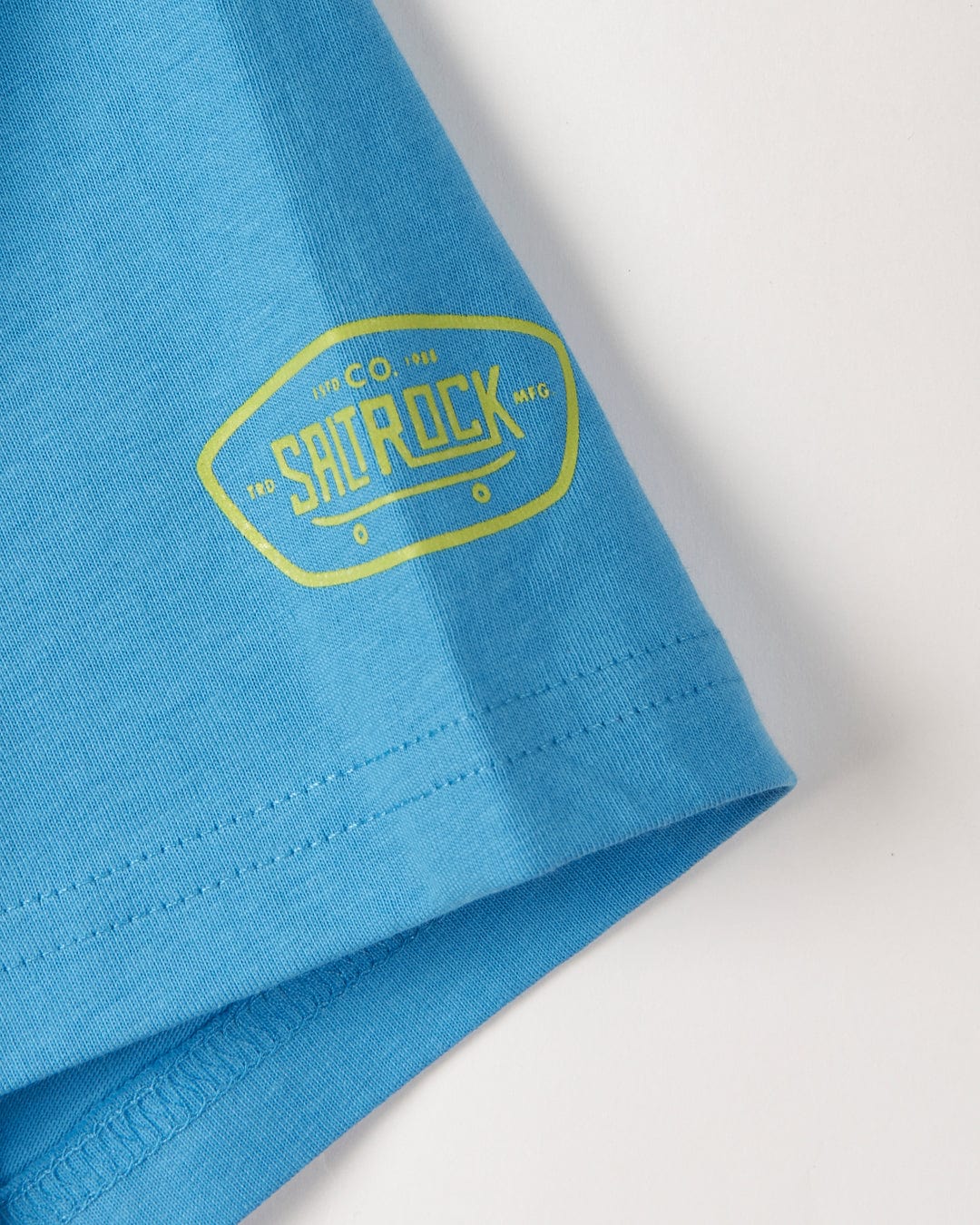 Close-up of a blue fabric with a 'Bowling for Surf - Kids Short Sleeve Glow in the Dark T-Shirt' logo on the hem by Saltrock.