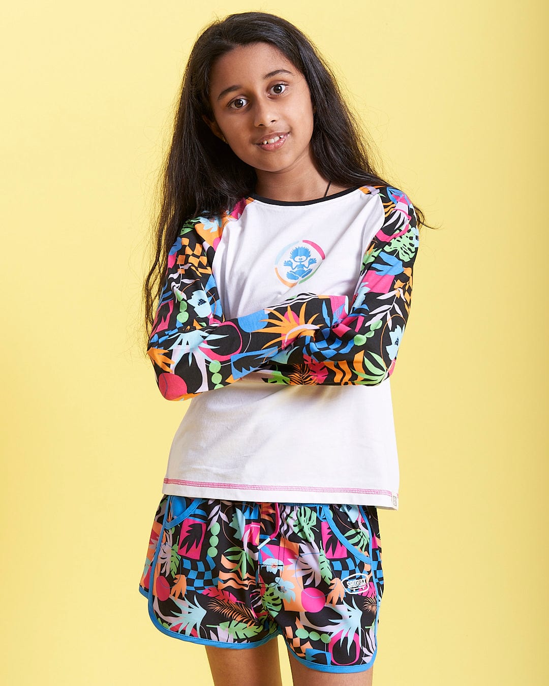 A young girl wearing a long - sleeved t - shirt and Saltrock Zephyr - Kids Boardshort - Blue.