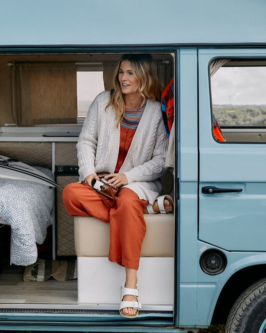 Smiling woman sitting in a retro camper van, wearing a chunky Cable - Womens Knitted Longline Cardigan in Cream by Saltrock.
