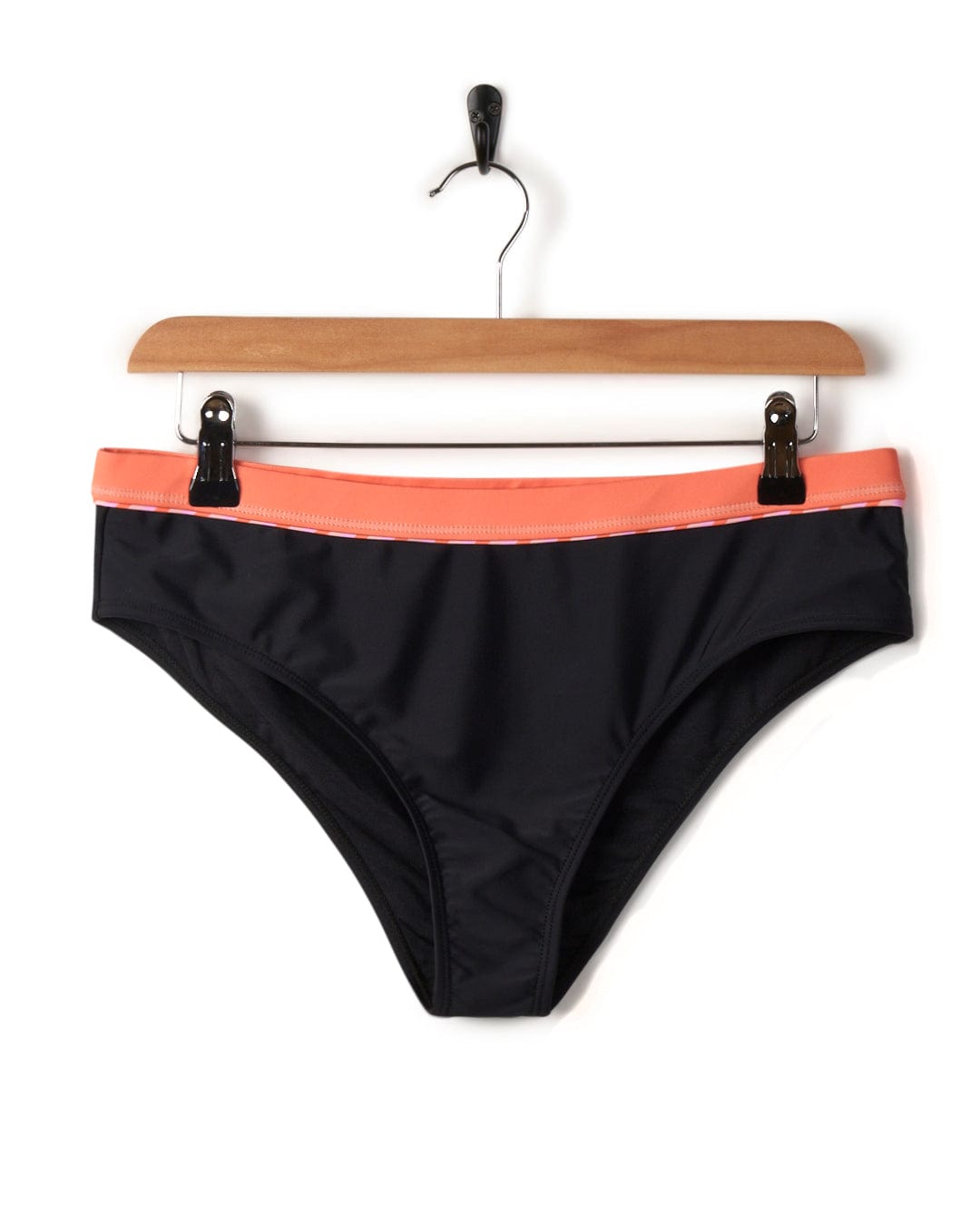 Caeley - Recycled Womens Retro Bikini Bottoms in Black by Saltrock, with an orange waistband, hanging on a wooden hanger against a white background.