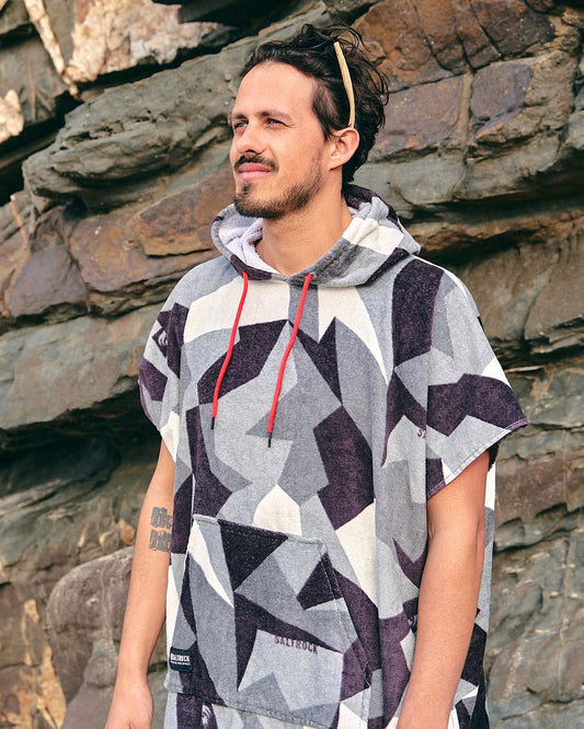 A man wearing a Saltrock Geo Camo - Changing Towel - Grey hooded poncho standing next to a rock.