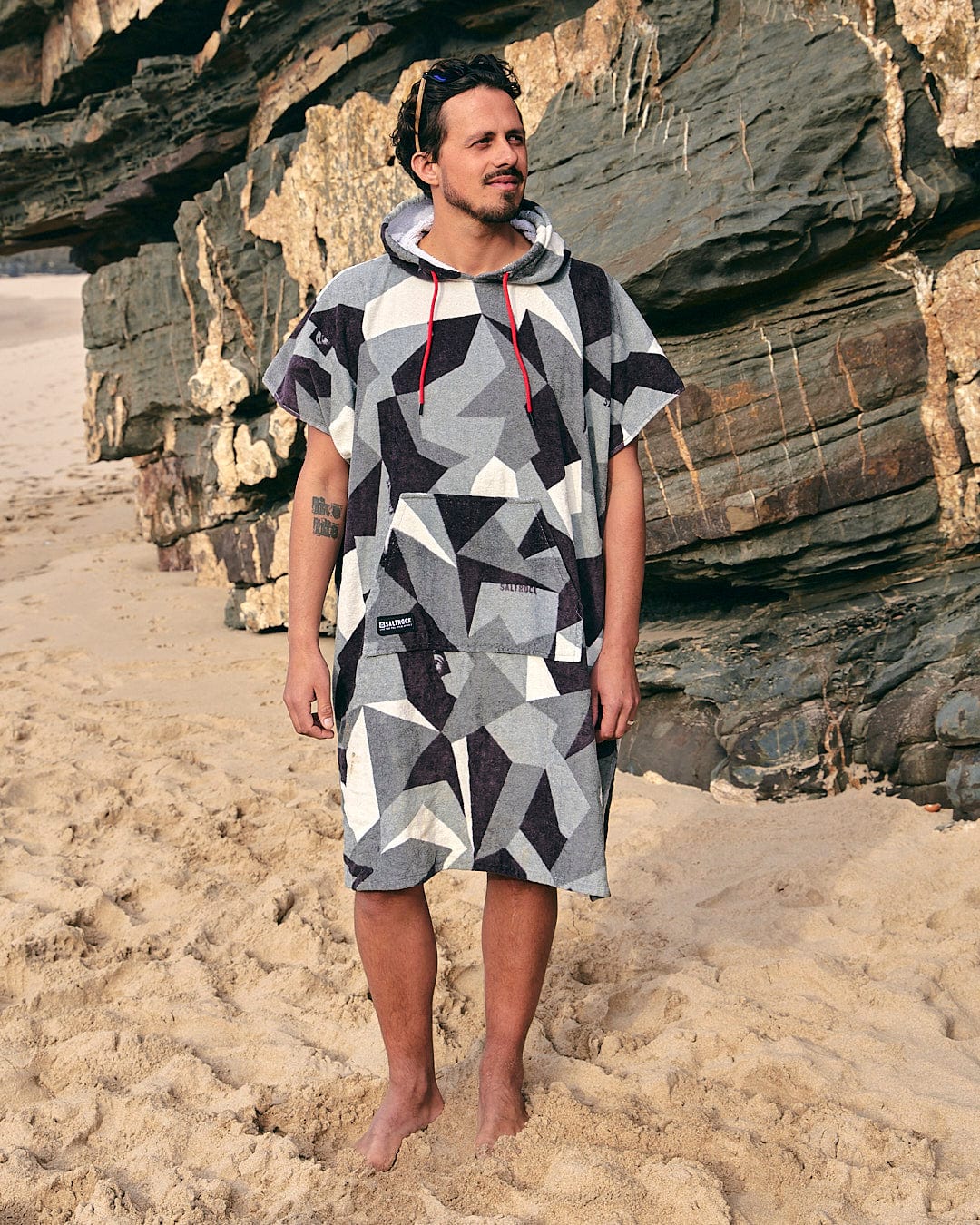 A man standing on a beach wearing a Saltrock Geo Camo - Changing Towel - Grey hoodie.