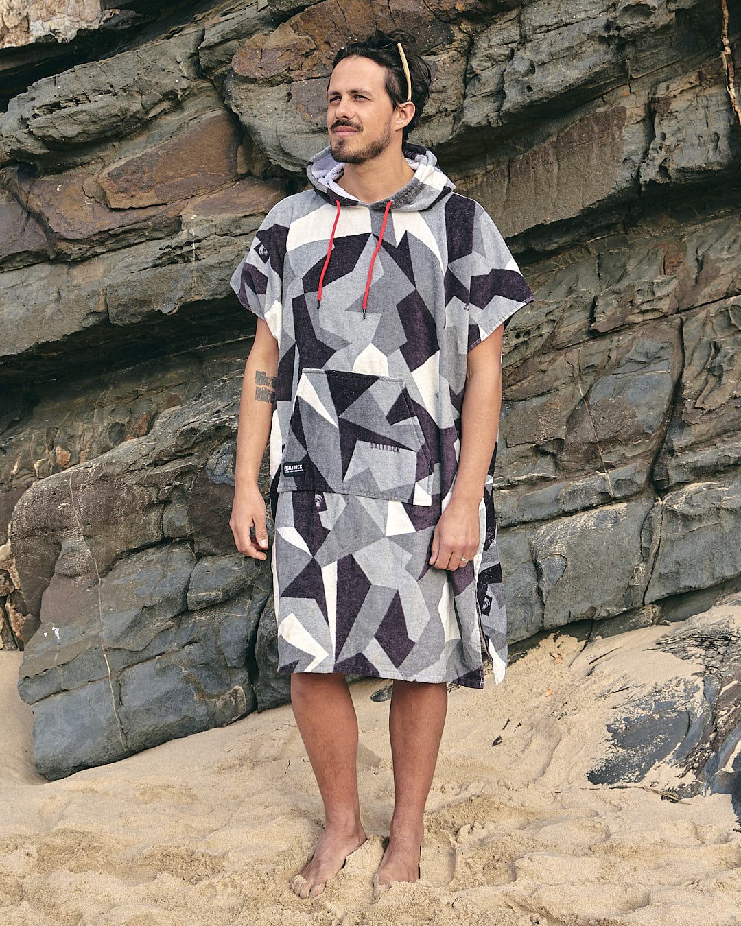 A man standing on the beach wearing a Geo Camo - Changing Towel - Grey hooded poncho made by Saltrock.
