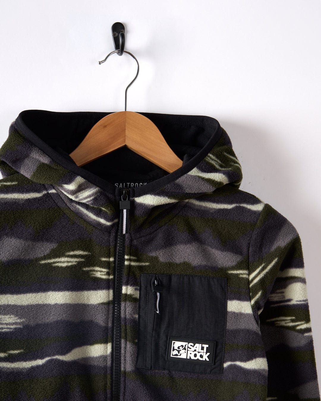 The "Camo Stripe - Kids Recycled Micro Fleece - Green" by Saltrock, featuring a front pocket and logo, is crafted from recycled materials and displayed on a wooden hanger against a white background.