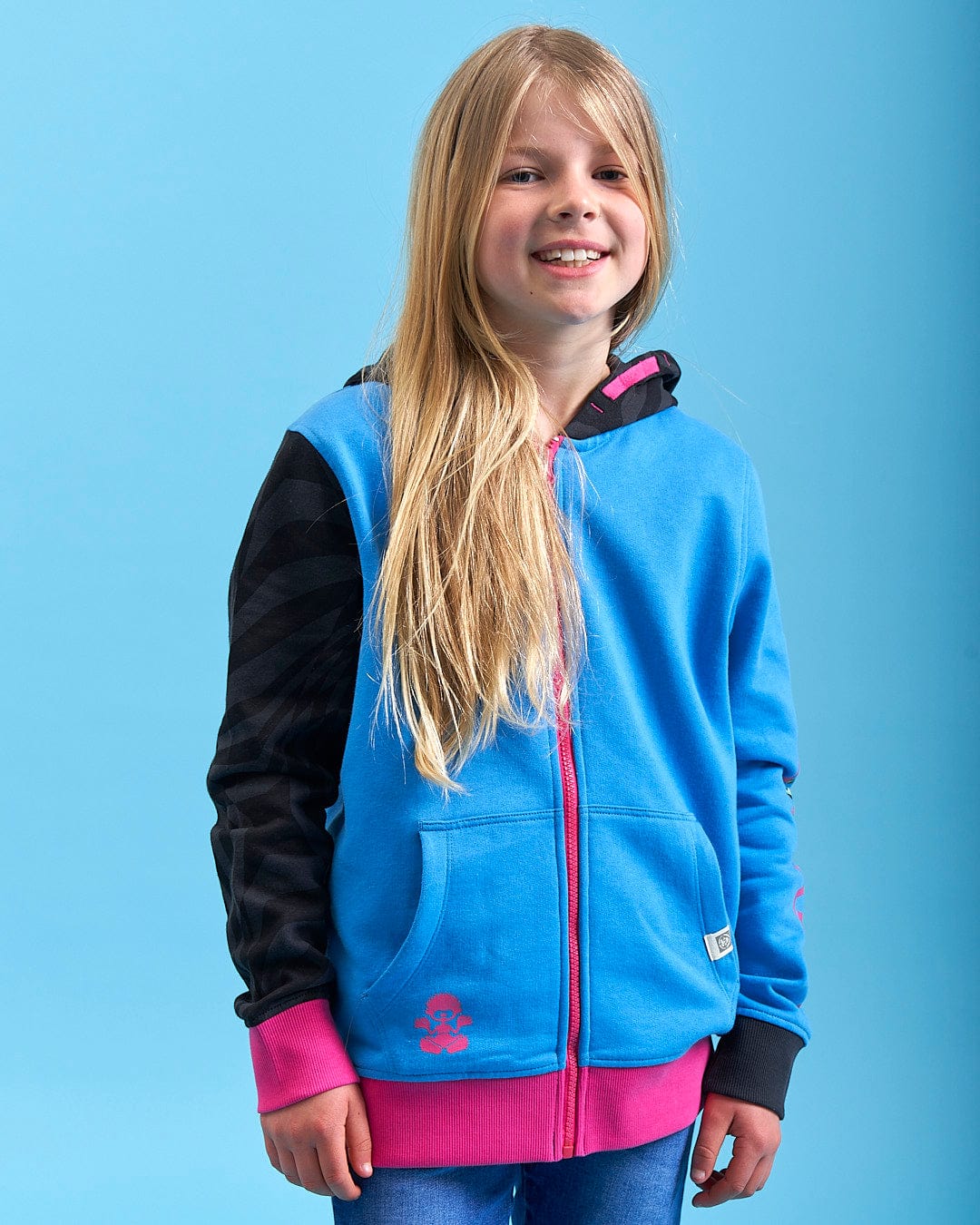 A young girl wearing a Saltrock Cara - Girls Zip Hoodie - Blue and jeans.