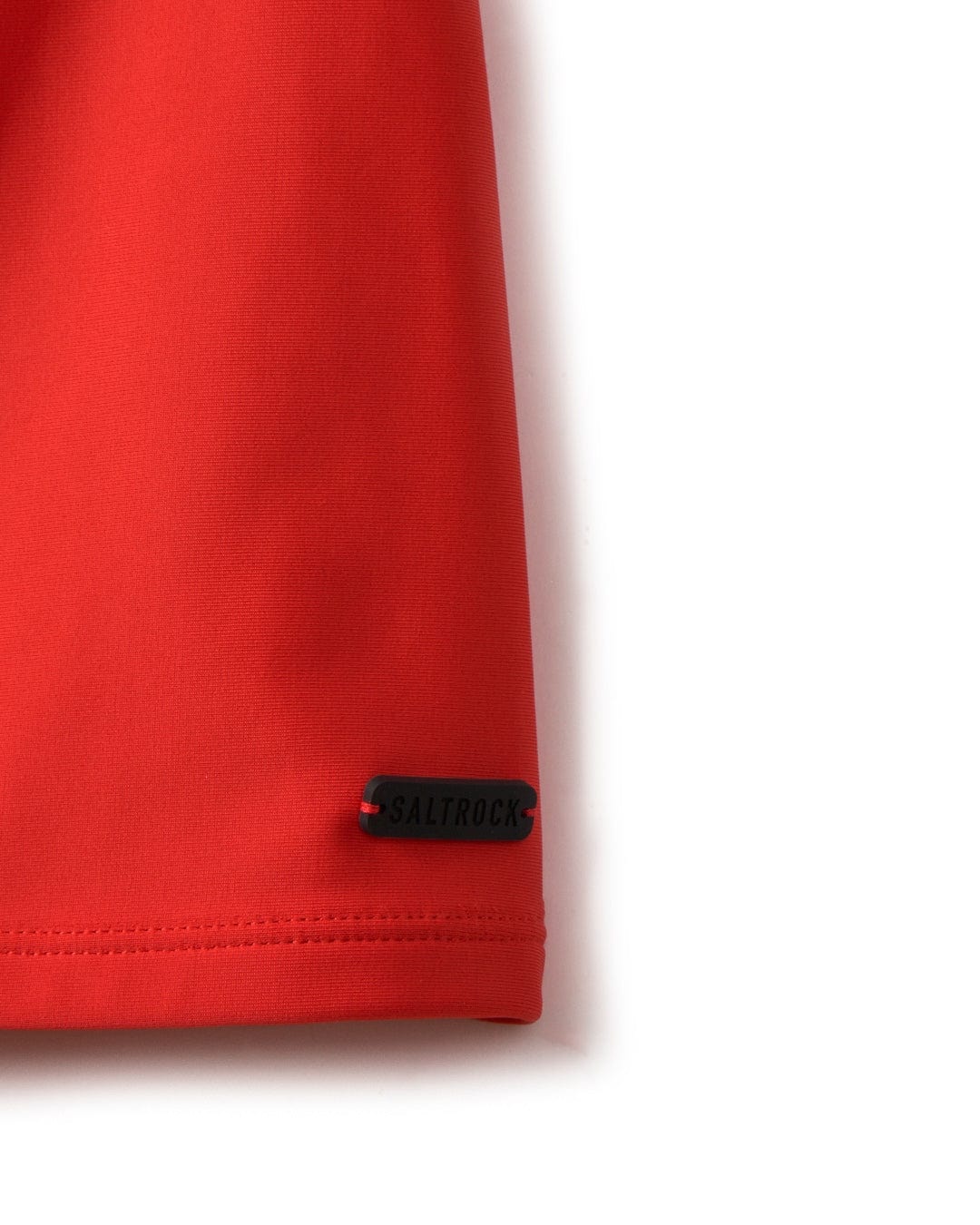 Close-up of a red fabric with a black "Saltrock" label on the hem, crafted from recycled fibers.