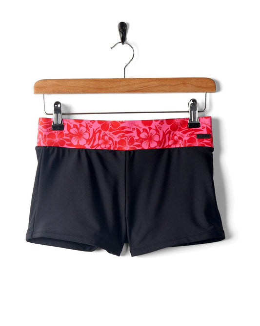 Cassie Hibiscus - Recycled Bikini Bottoms - Black/Pink with an elasticated red Hibiscus print waistband, made from recycled fibres, hanging on a wooden hanger by Saltrock.