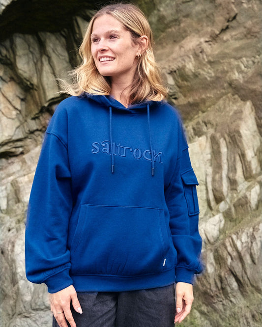 A woman wearing a blue Celeste - Womens Pop Hoodie - Blue with embroidered Saltrock branding.