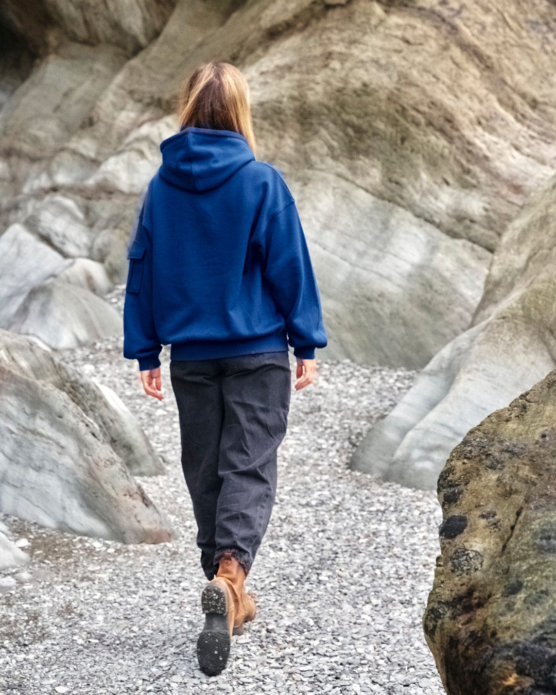 A woman wearing a Celeste - Womens Pop Hoodie - Blue by Saltrock, walking on a rocky path near rocks.