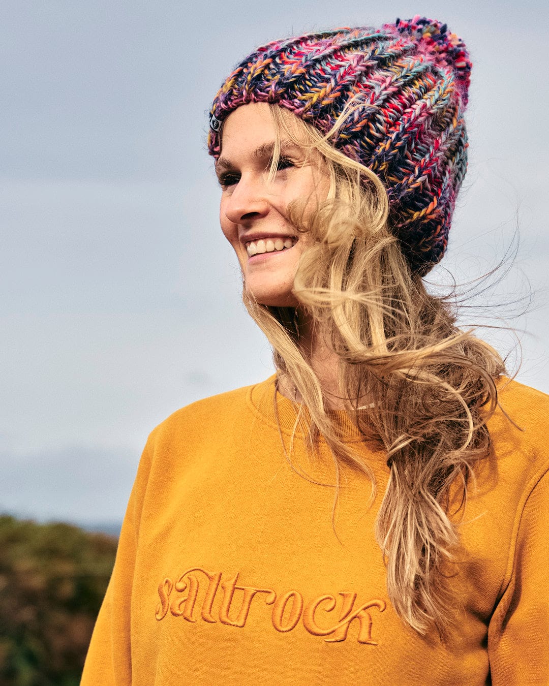 A blonde woman wearing a colorful knitted Celeste - Womens Sweat - Yellow hat made from a cotton-polyester blend fabric. (Brand Name: Saltrock)
