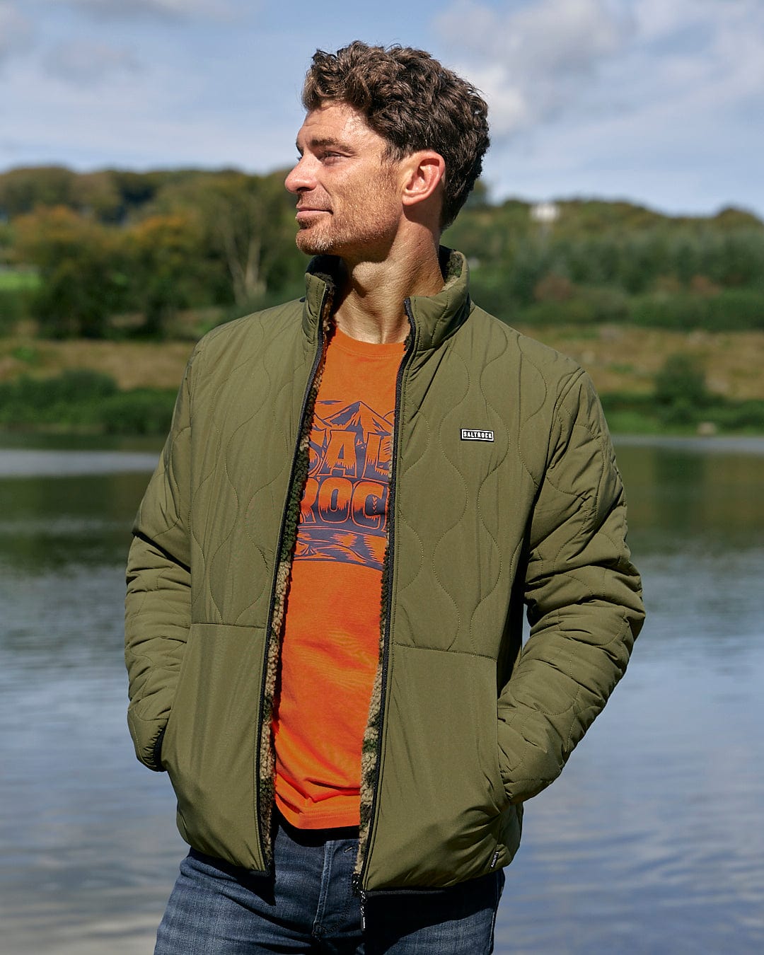 A man wearing a Saltrock Cirrus - Quilted Reversible Jacket - Dark Green and orange t-shirt.
