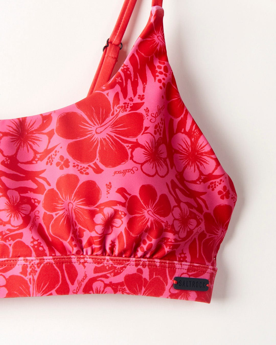 Close-up of a red and pink floral bikini top made from recycled fibres, with adjustable straps and featuring the brand logo "Saltrock" on a small black tag at the bottom hem.