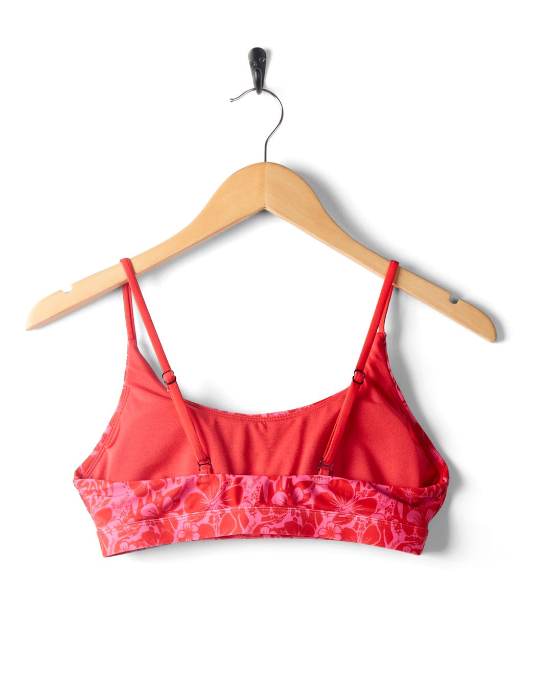 A Cleo Hibiscus - Recycled Bikini Top - Pink from Saltrock with adjustable straps and a floral pattern, made from recycled fibres, is hanging on a wooden hanger against a white background.