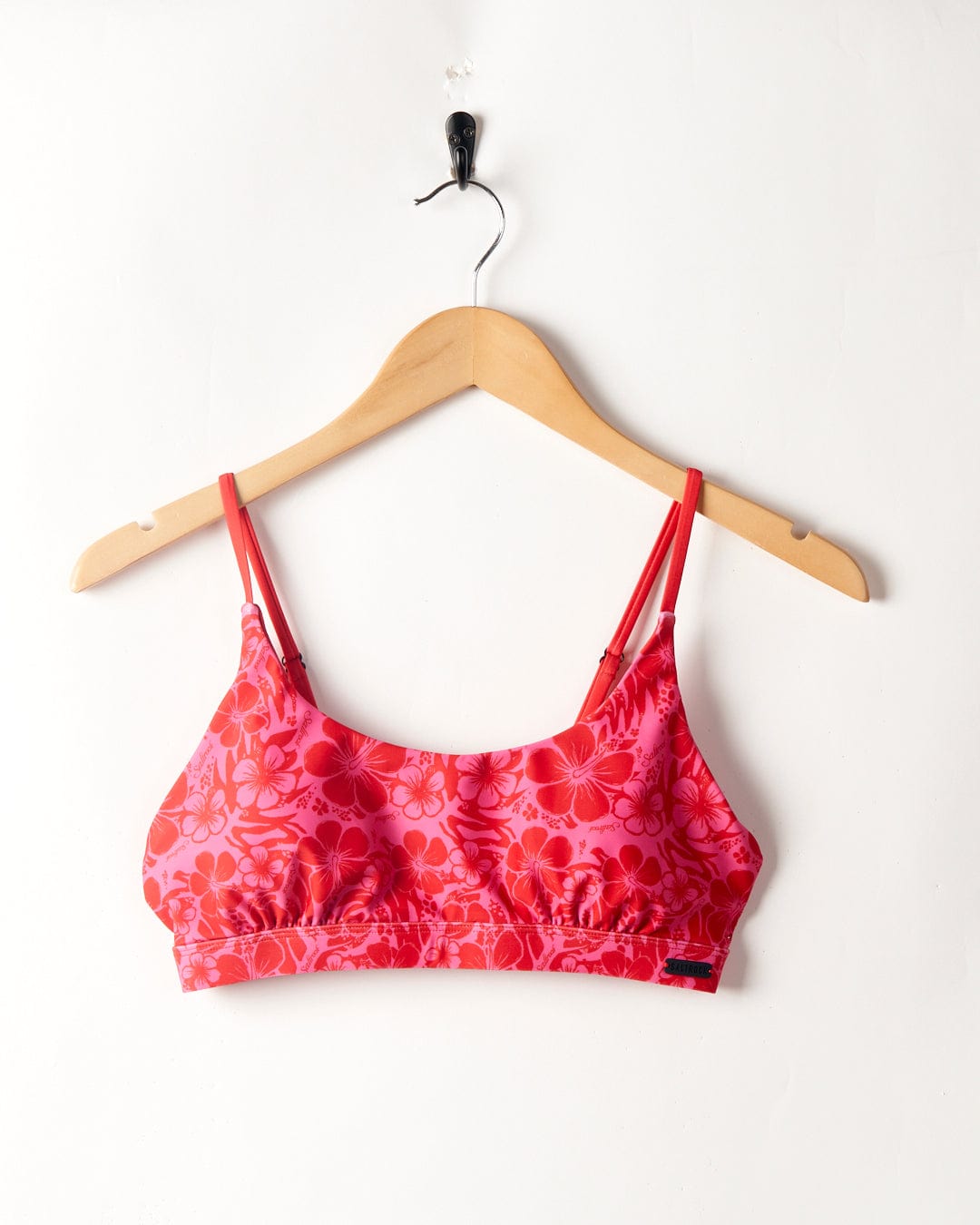 Cleo Hibiscus Saltrock - Recycled Bikini Top - Pink hanging on a wooden hanger against a white wall.