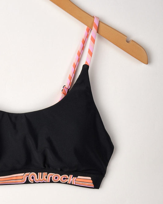 Cleo - Recycled Womens Retro Bikini Top - Dark Grey sports bra with peach striped adjustable straps and an orange striped Saltrock logo, hanging on a wooden hanger against a white background.