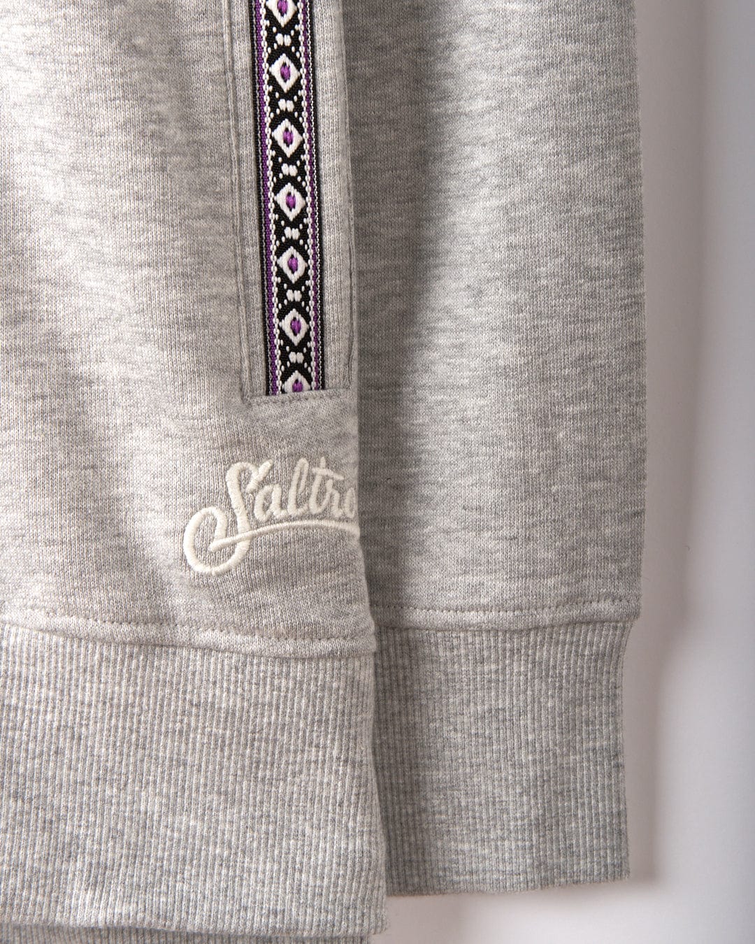 Close-up of the Saltrock Cliffden Women's Pop Hoodie in grey, featuring ribbed cuffs, a vertical ribbon detail, and "Saltrock" embroidery near the pocket. This cotton hoodie offers both style and comfort.
