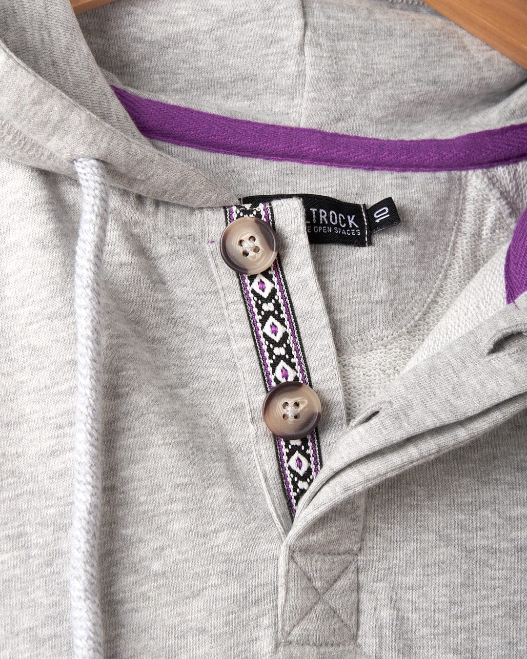 Close-up of the Saltrock Cliffden Womens Pop Hoodie in grey, featuring two beige buttons, a purple and black patterned trim, and a black "10" size tag on the collar.