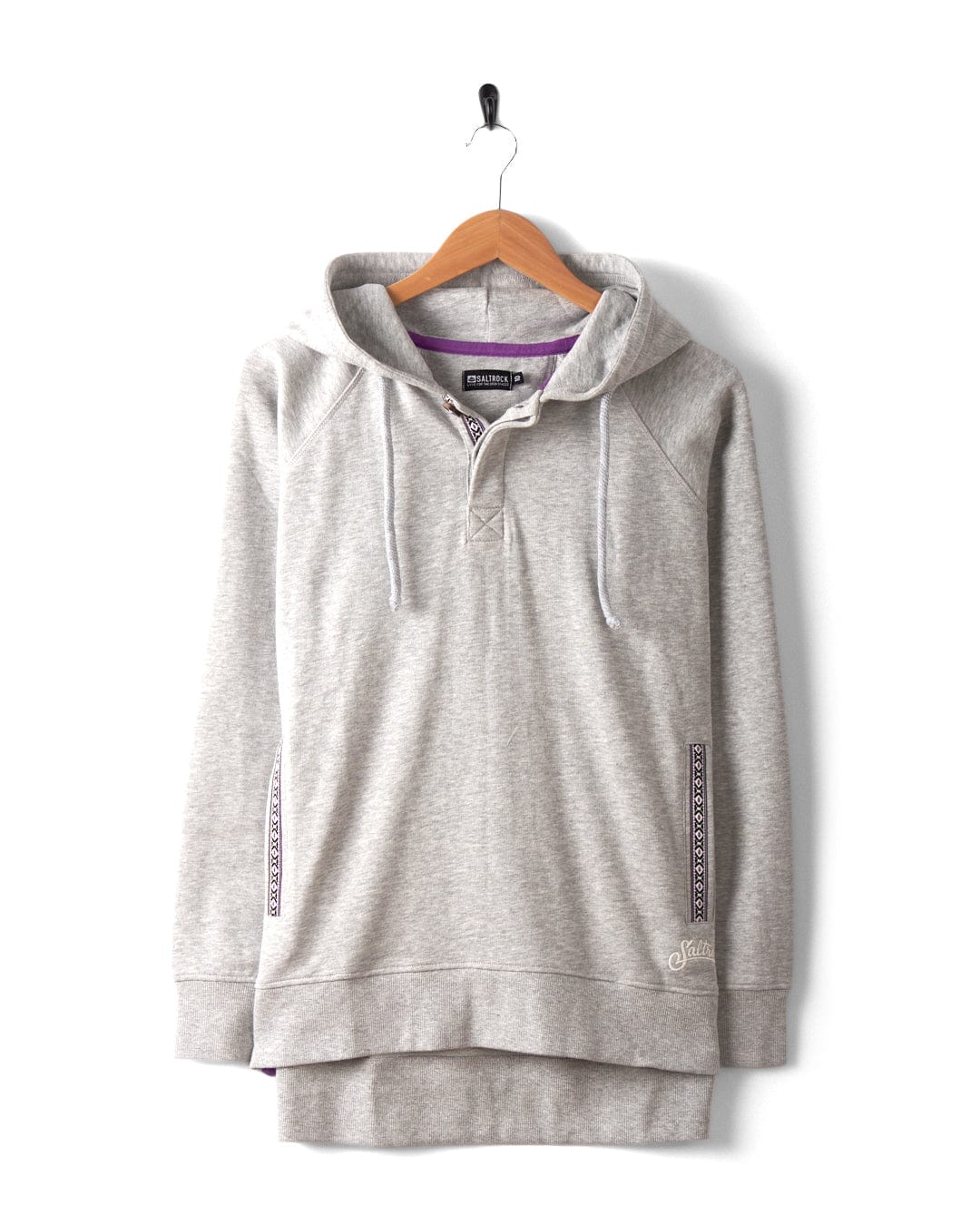 The Saltrock Cliffden Women's Pop Hoodie in grey features drawstrings, a partial button placket, and patterned trim. Displayed on a wooden hanger against a white background, this machine-washable hoodie offers comfort and style for everyday wear.