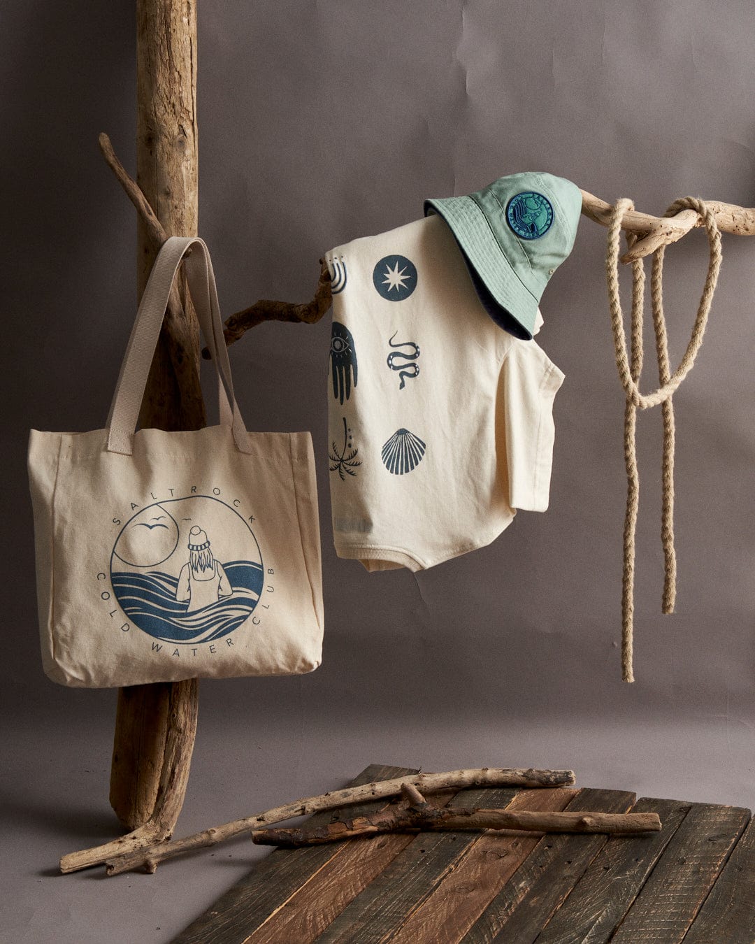 Eco-friendly apparel and accessories with marine-inspired designs, including Cold Water Club recycled shopper bags in cream color, displayed on a rustic wooden stand by Saltrock.