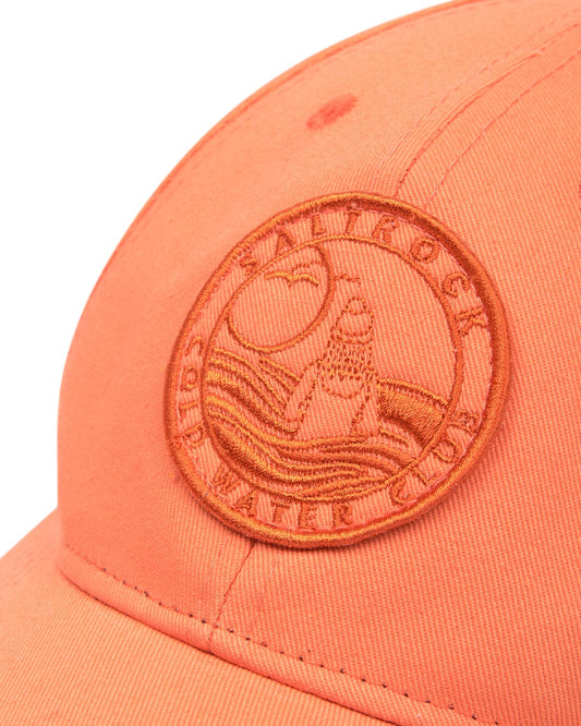 Close-up of a coral-colored Saltrock Cold Water Club cap with a curved visor and a circular embroidered logo.