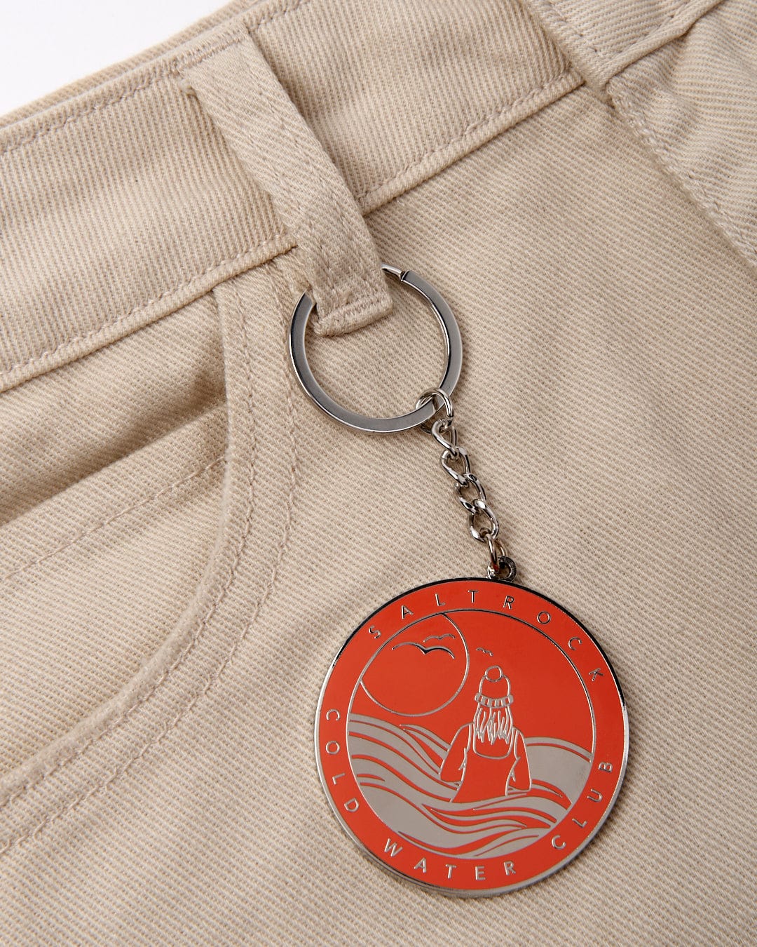 Keychain with a Saltrock "Cold Water Club" circular logo attached to a belt loop of beige trousers.