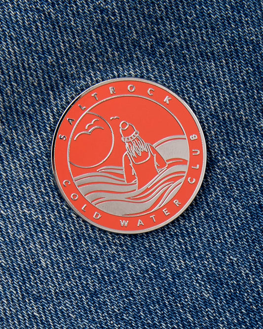 A red and silver Saltrock Cold Water Club pin with a safety clasp attached to denim fabric.