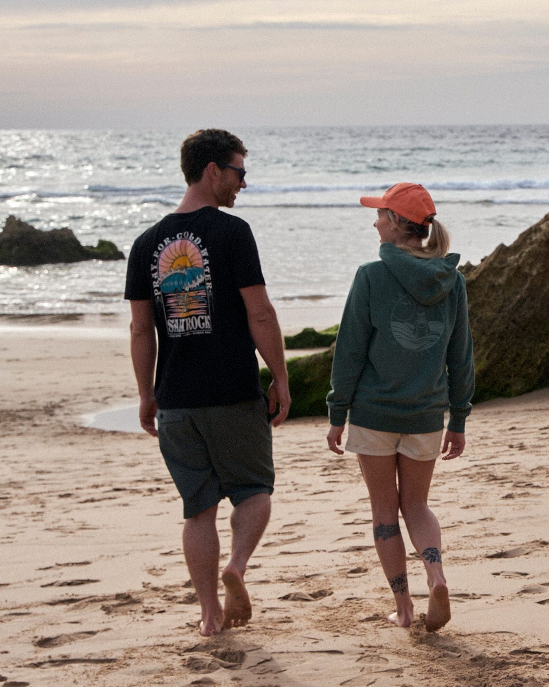 A man and woman walking on a beach wearing Saltrock Cold Water - Mens Short Sleeve T-Shirt - Black clothing.