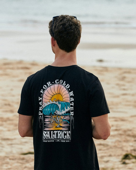 The back of a man standing on the beach wearing a Saltrock Cold Water - Mens Short Sleeve T-Shirt in Black.