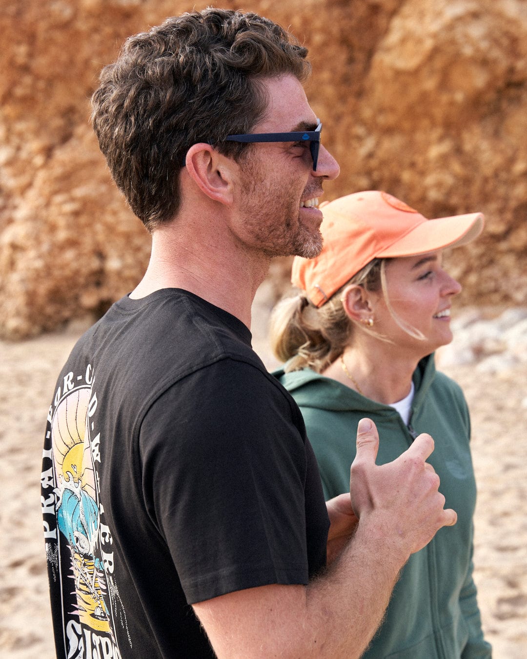 A man and a woman standing on a beach, wearing Saltrock Cold Water - Mens Short Sleeve T-Shirt - Black clothing.