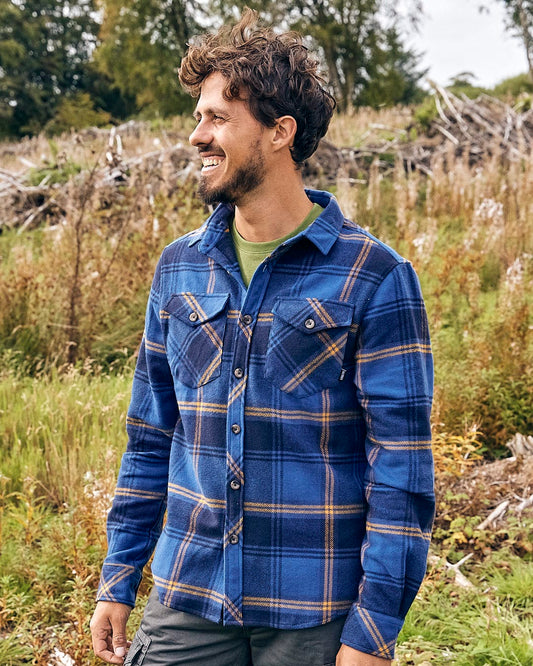 A man wearing a Saltrock Colter - Mens Hooded Shirt in Blue and yellow plaid in a field made from high quality fabric.