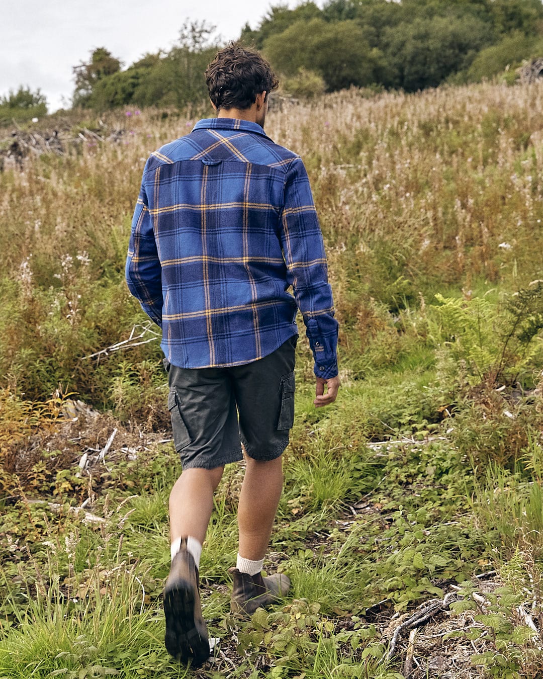 A man walking through a grassy field wearing a Saltrock Colter - Mens Hooded Longsleeve Shirt in Dark Blue.