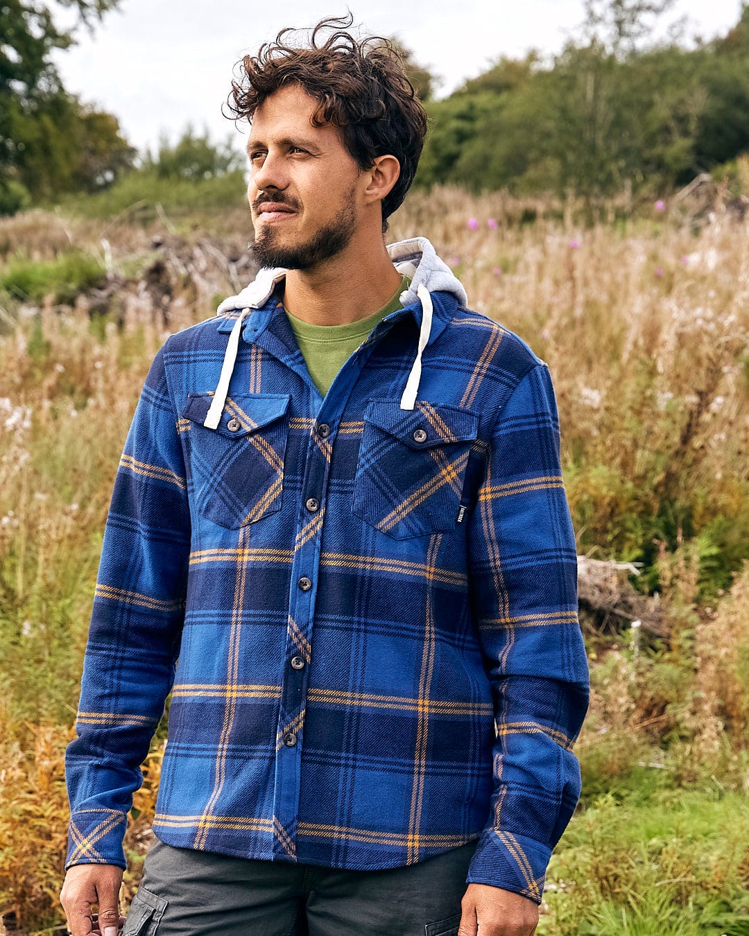 A man in a Saltrock Colter - Mens Hooded Longsleeve Shirt - Dark Blue standing in a field.