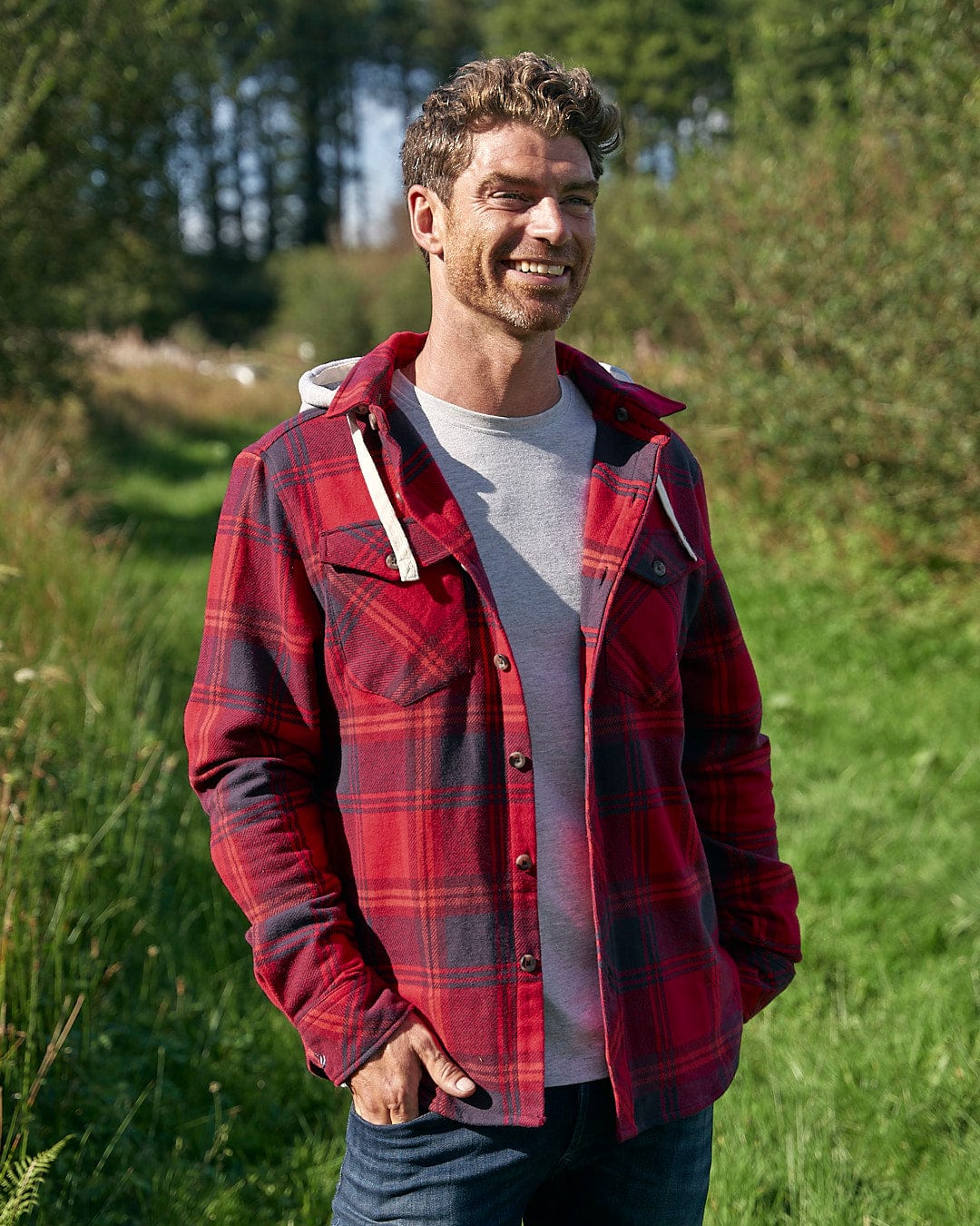 A man in a Saltrock Colter - Hooded Long Sleeve Shirt - Red standing in a field.