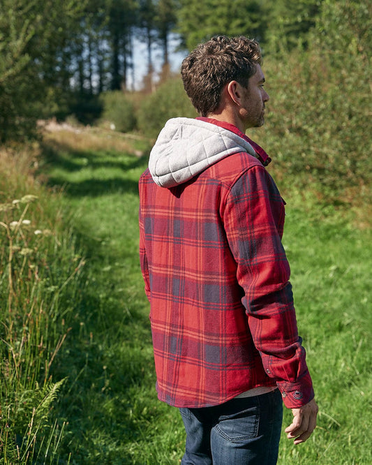 A man in a Colter - Mens Hooded Shirt in Red plaid (check fabric) standing in a field.