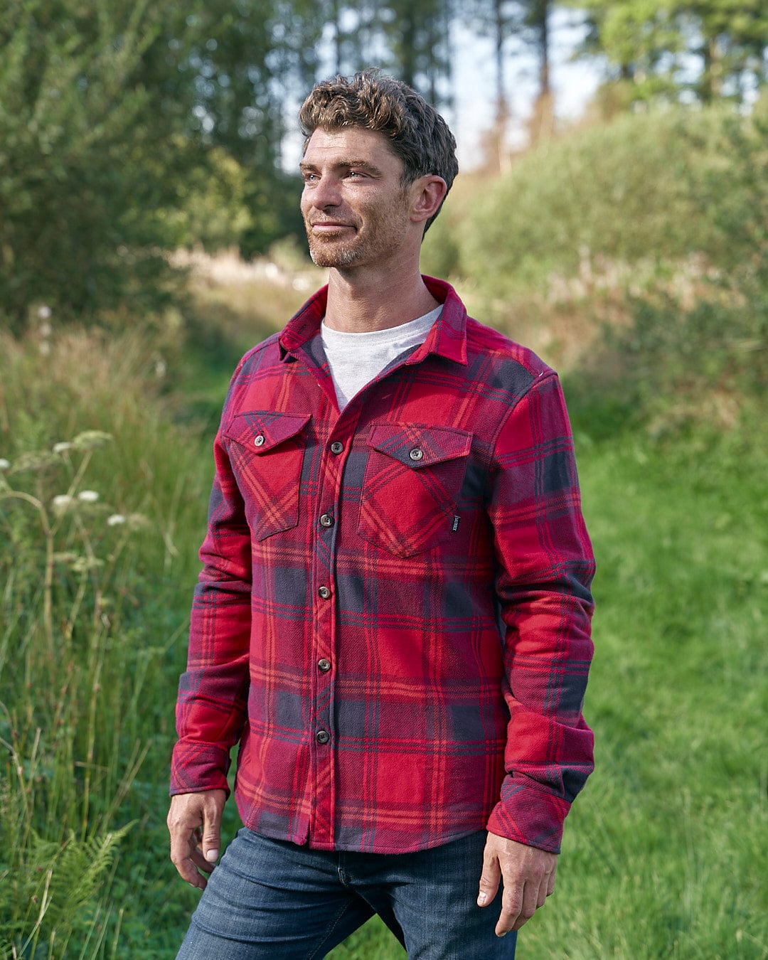 A man in a Saltrock Colter - Hooded Long Sleeve Shirt - Red standing in a field.