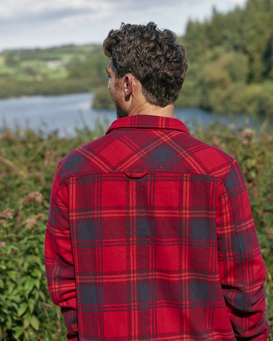 A man wearing a red Saltrock Colter Hooded Shirt looking at a lake.