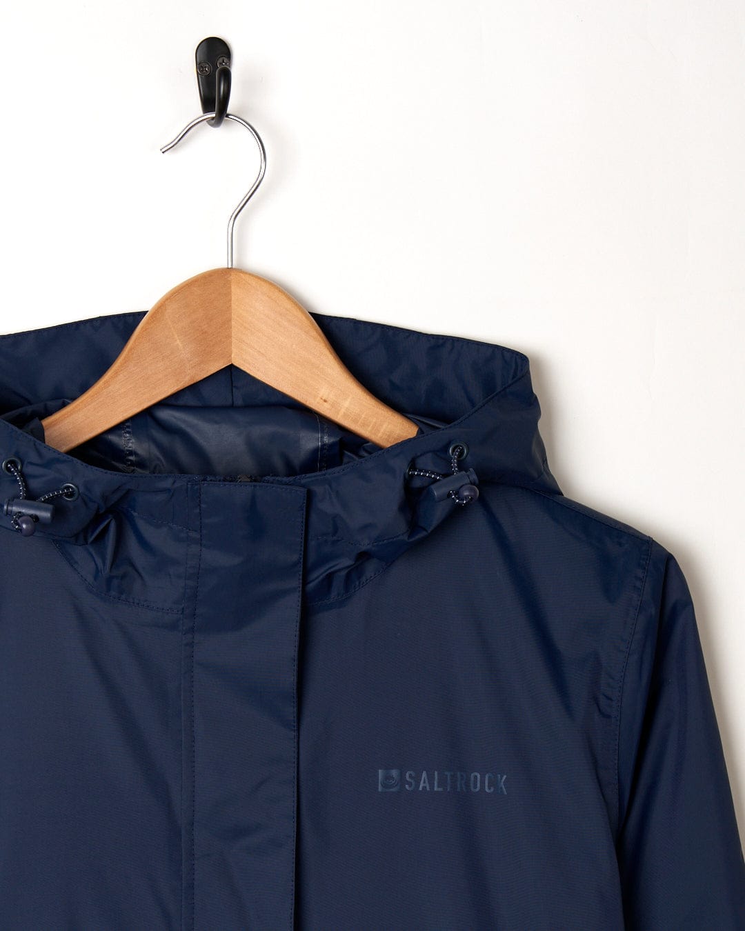 A dark blue waterproof Saltrock Cooper - Womens Packable Waterproof Jacket hanging on a wooden hanger against a white background.