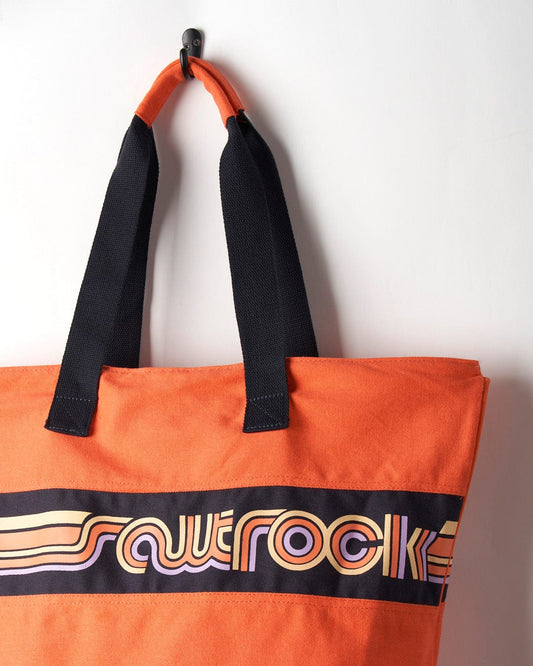 Coral Saltrock Cora Retro Beach Bag with black straps hanging on a hook against a white wall.