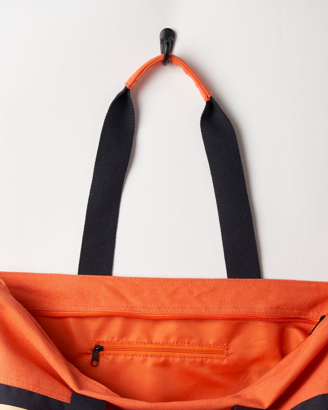 A close-up view of an open coral Saltrock Cora Retro Beach Bag with durable branding and an adjustable strap hanging from a hook.