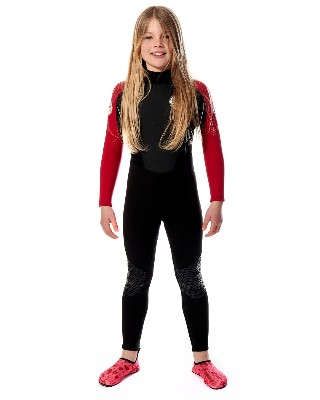 A young girl in a Saltrock Core - Kids 3/2 Full Wetsuit - Black/Red posing for a photo.