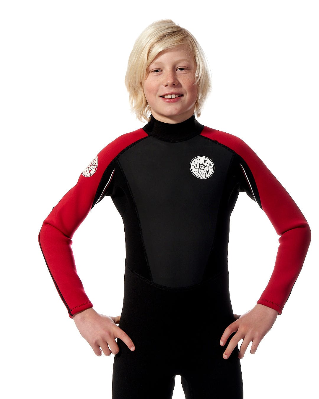 A young boy in a Saltrock Core - Kids 3/2 Full Wetsuit - Red posing for a photo.