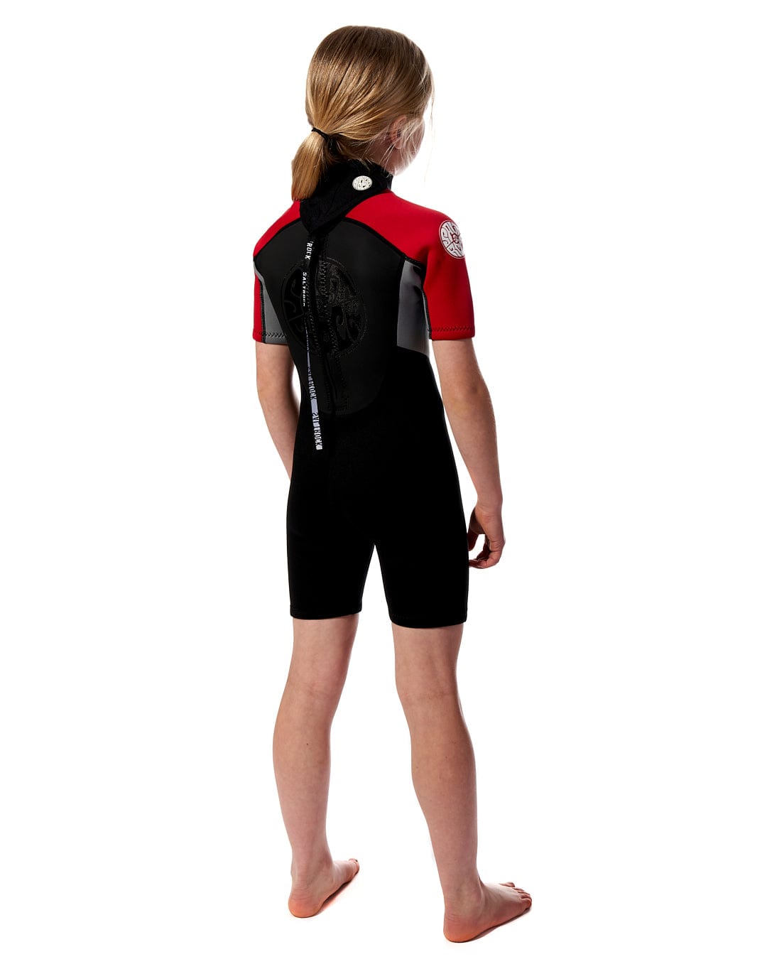 A girl in a black and red Saltrock Core - Boys 3/2 Shortie Wetsuit at the beach.