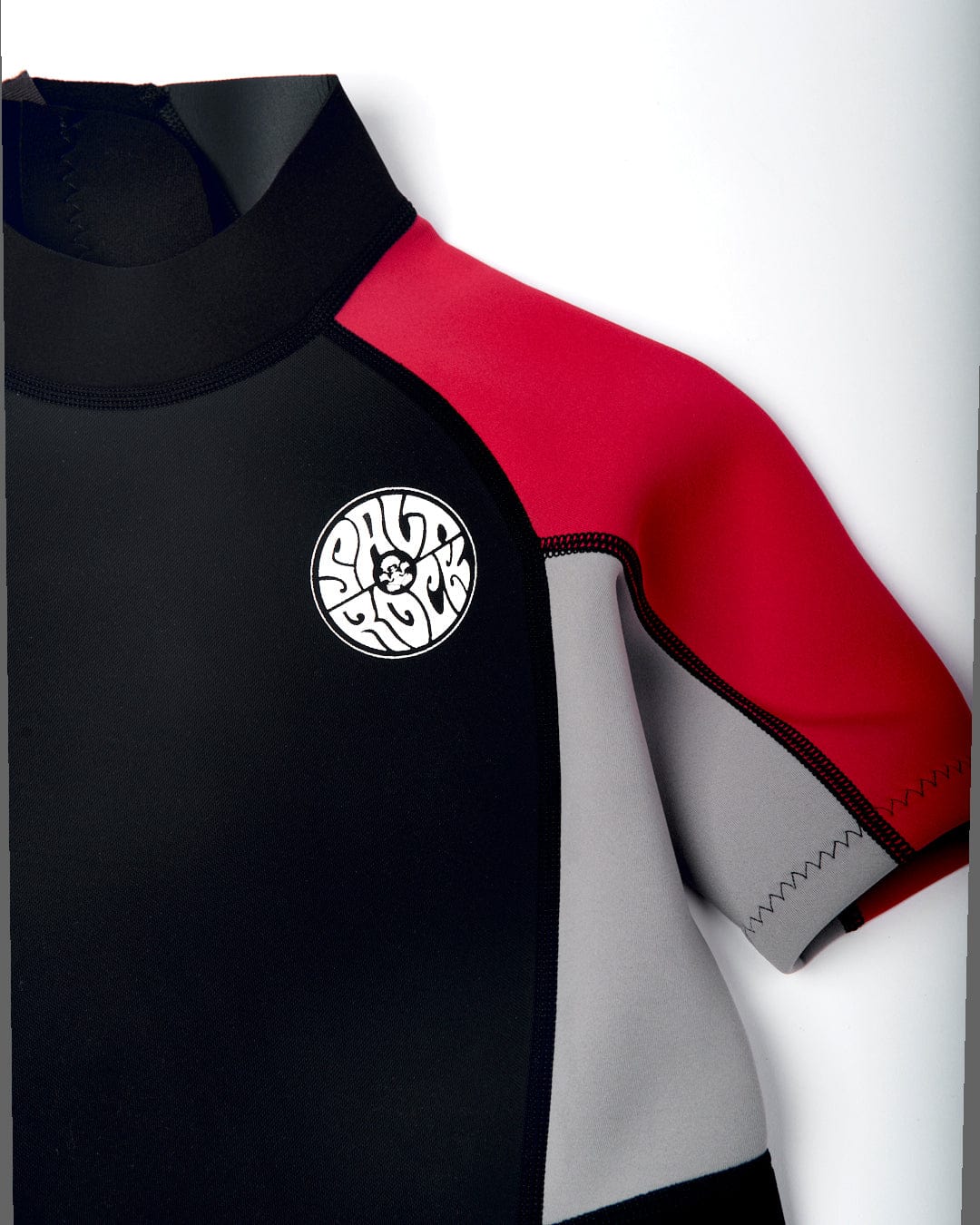 Close-up of a black neoprene Saltrock wetsuit with red and grey sleeve accents and a circular white logo on the chest.
