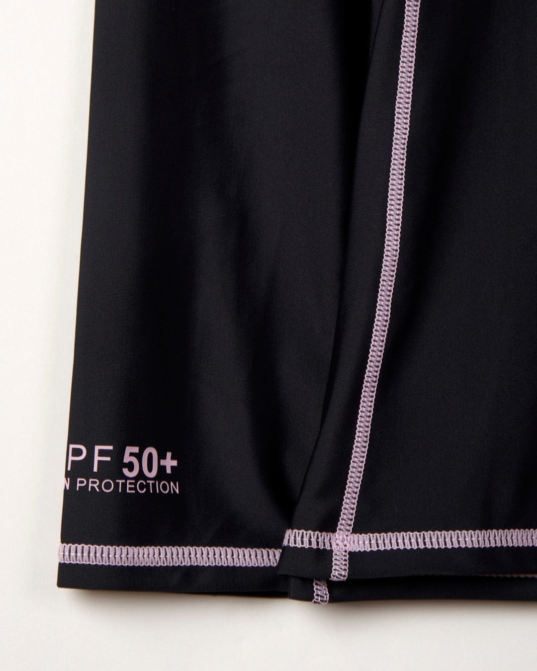 Close-up of Saltrock's Core - Recycled Women's Long Sleeve Rashvest in black fabric with "UPF 50 Protection" label and purple flat locked stitching.