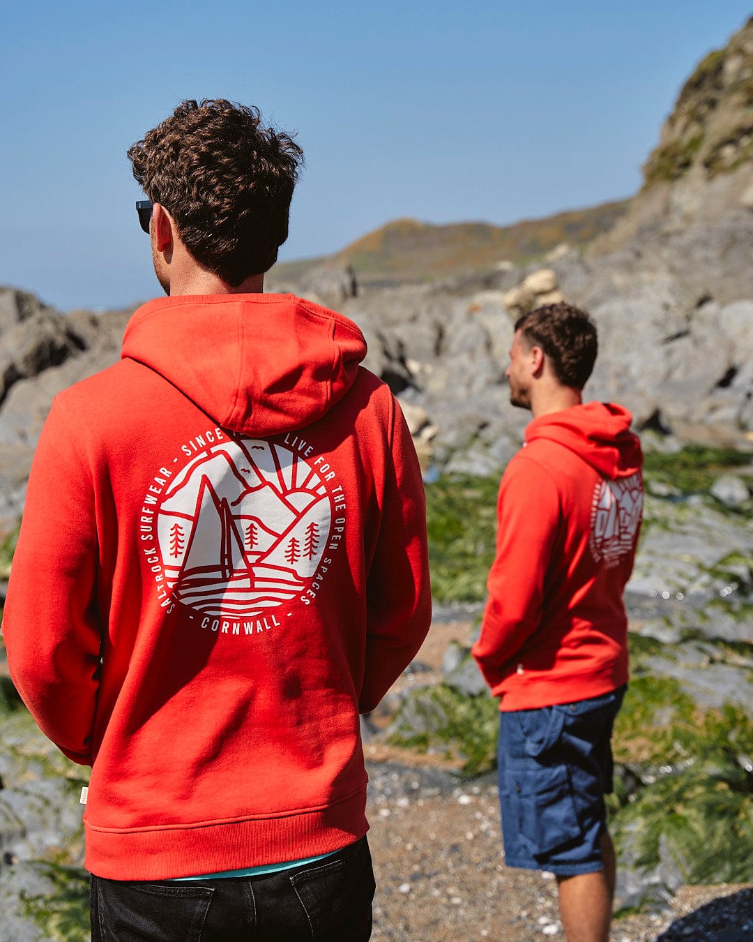 Two men in Saltrock hoodies standing on a rocky beach.