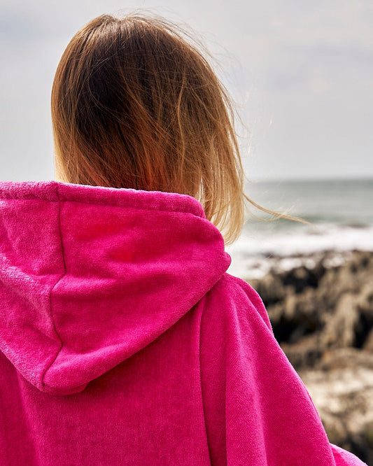 A person in a pink Saltrock Corp Changing Towel - Bright Pink hoodie, looking out towards the sea.