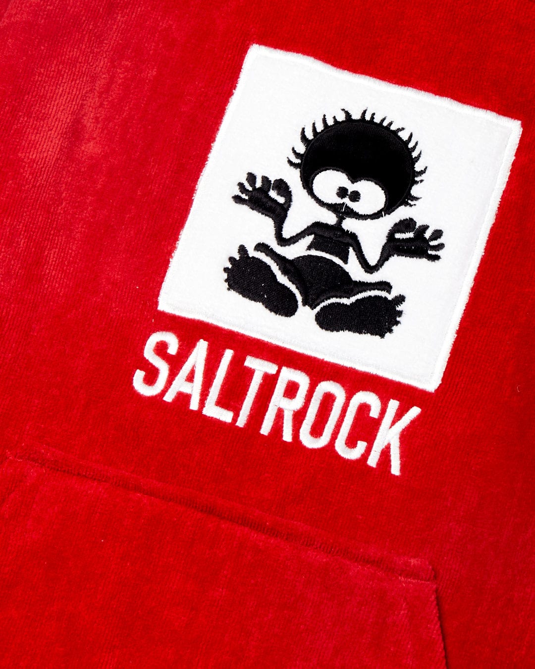 White logo of a stylized sun figure on a red 100% cotton towel background with the word "Saltrock" in white text.