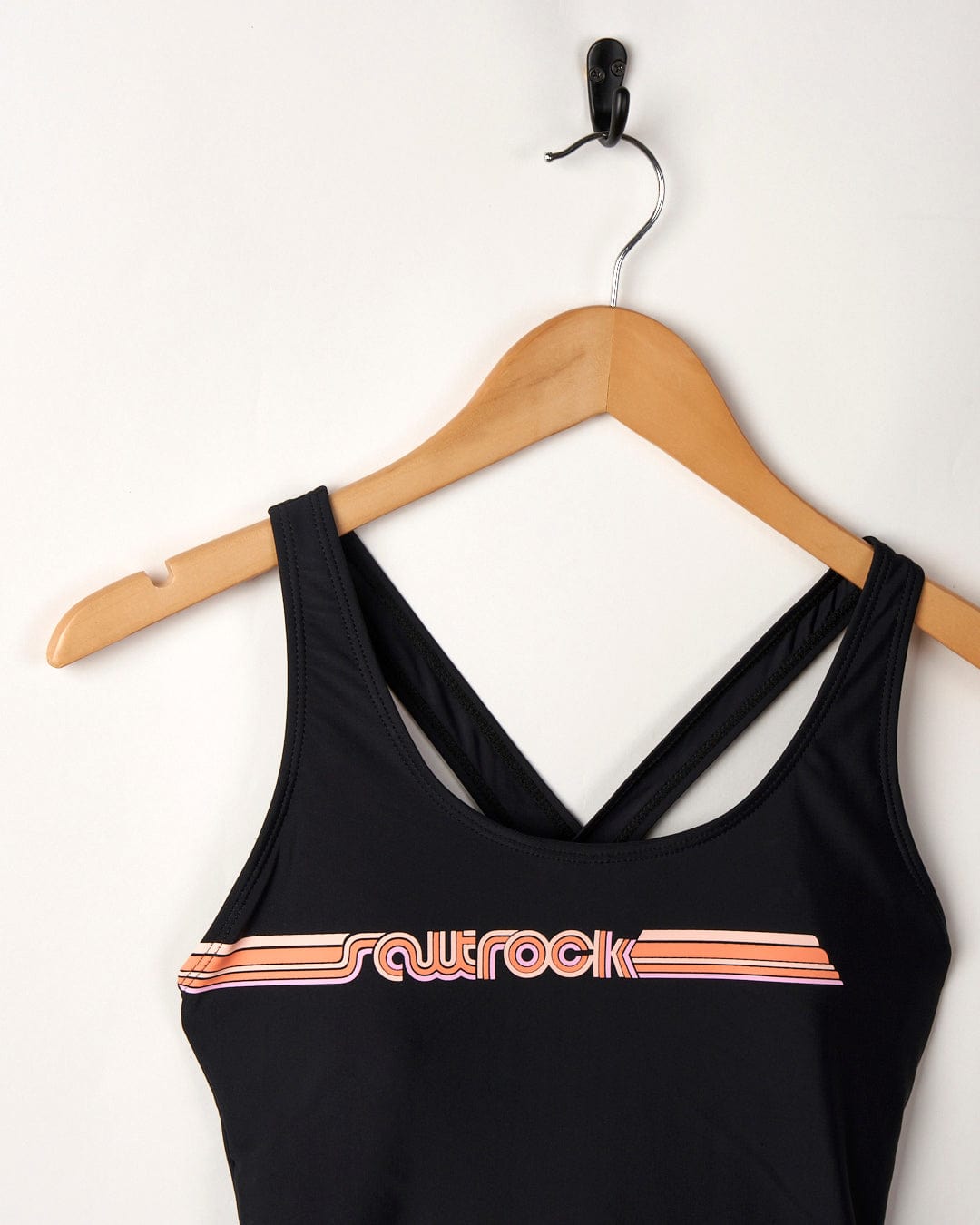 Corrine Retro swimsuit in black with orange stripe detail, made from recycled fibres, hanging on a wooden hanger against a white wall.